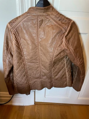 Brun skinnjacka med fuskpälsfoder - Snygg brun skinnjacka med mjukt fuskpälsfoder på insidan. Jackan har dragkedja, markerade sömmar och en cool bikerinspirerad look. Perfekt för dig som vill ha en stilren men ändå edgy jacka ig