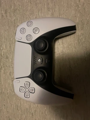 Vit PlayStation 5 DualSense handkontroll - Säljer en snygg och modern vit DualSense handkontroll till PlayStation 5. Kontrollen har svart detaljdesign, klassiska PlayStation-knappar och två analoga spakar. Ergonomisk form och tillverkad i plast för bästa grepp.