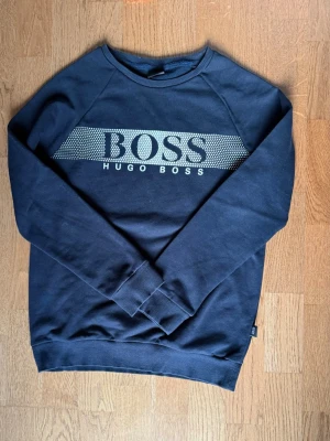 Svart sweatshirt från Hugo Boss - Snygg svart sweatshirt från Hugo Boss med stort vitt tryck över bröstet. 