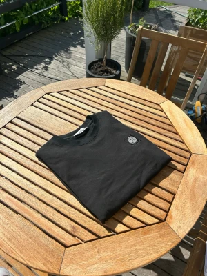 Svart Stone Island t-shirt - Svart t-shirt från Stone Island med klassisk rund hals och logopatch på bröstet. Enkel och stilren design som passar perfekt till jeans eller shorts. Materialet är mjuk bomull och modellen har korta ärmar.