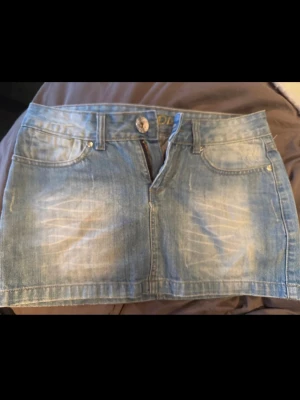 Ljusblå lågmidjad jeanskjol  - Snygg ljusblå jeanskjol med slitningar framtill och broderade detaljer på bakfickorna. 