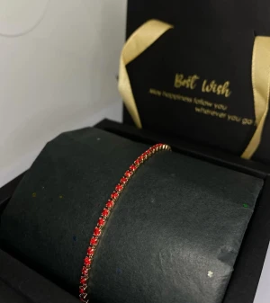 Tennisarmband med röda diamanter - Snyggt tennisarmband i guldton med små röda diamanter som ger en elegant och trendig look. Perfekt för dig som vill ha en färgklick på handleden. Armbandet har en tunn och smidig design som gör det lätt att bära och matcha med andra smycken.
