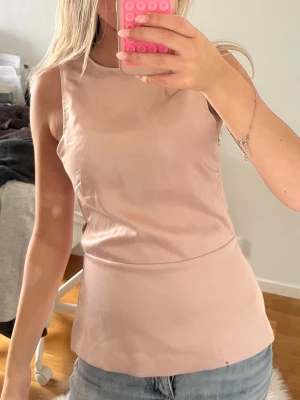 Ljusrosa ärmlös topp  - Säljer en ljusrosa, ärmlös topp med snygga öppna detaljer på sidorna. Toppen har en figurnära passform och är tillverkad i ett slätt material som ger en stilren look. Perfekt för dig som vill ha något enkelt men ändå trendigt.