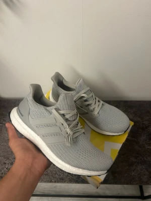 Grå Adidas Ultraboost sneakers - Snygga grå Adidas Ultraboost sneakers med stickad ovandel i mesh och klassiska tre ränder på sidan. Skorna har vit Boost-sula för extra komfort och svart yttersula. Perfekta för dig som gillar stilrena och bekväma sneakers.
