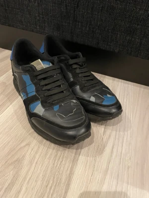 Svarta och blå sneakers från Puma - Snygga sneakers från valentino i svart och blå camo- färg. Skorna är i väldigt bra skick och används få gånger pga att dom har suttit lite tajt på mig. Inget fel på dom. Dom är väldigt sköna och ser väldigt bra ut.