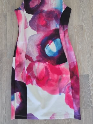 Färgstark mönstrad klänning i stretch - Snygg ärmlös klänning med färgstarkt abstrakt mönster i rosa, lila, blått och vitt. Kroppsnära passform och rund halsringning. Perfekt för dig som vill sticka ut med en unik look. Materialet känns mjukt och stretchigt, vilket ger en bekväm känsla hela dagen.