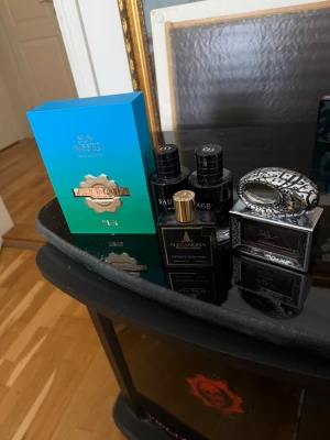 Mix av exklusiva parfymer - Säljer ett set med lyxiga parfymer: Alexandria Fragrances i svart flaska med gulddetaljer, två flaskor Dior Sauvage i svart, Ajmal Silver Shade i silverfärgad flaska med dekorativ kork och en Sea Kissed parfym i turkos förpackning. Perfekt för dig som gillar unika dofter. Byter säljer 