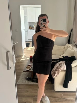 Svart oneshoulder kort klänning - Snygg svart kort klänning med oneshoulder-design. Klänningen har en figurnära passform och är perfekt för dig som gillar en stilren och modern look. Enkel och elegant modell som framhäver axlarna.