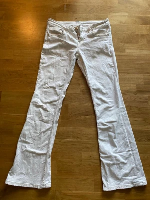 Vita bootcut jeans med fickdetaljer - Säljer ett par vita bootcut jeans med snygga fickdetaljer och knappar. Jeansen är lågmidjade och är i storlek 38