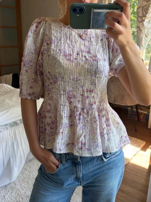 Blommig topp med puffärm - Supersöt blus med puffiga korta ärmar och volang nedtill.