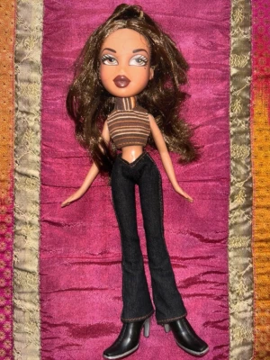 Vintage Bratz docka Y2K outfit tidigt 2000-tal - Vintage Bratz-docka Yasmin från tidigt 2000-tal med klassisk Y2K-look. Dockan har långt brunt hår, randig crop top, mörka bootcut jeans och svarta boots enligt bilder.  Perfekt för samlare eller dig som älskar Bratz och tidigt 2000-talsmode.  Skick: mycket bra begagnat skick Märke: Bratz (MGA)