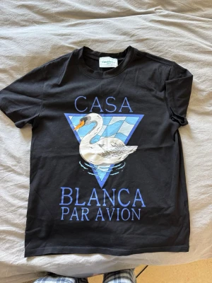 Casa Blanca t-shirt  - Svart t-shirt från Casablanca med stor grafisk print framtill som visar en vit svan och texten 'Casa Blanca Par Avion' i blått. Klassisk rund hals och korta ärmar. Tillverkad i mjuk bomull för skön känsla.