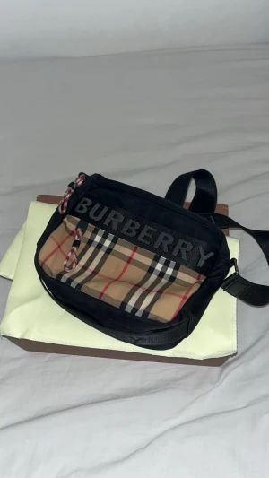 Burberry axelväska - Säljer en snygg axelväska från Burberry med det ikoniska rutmönstret i beige, svart och rött. Den är knappt använd jätte bra skick. Pris kan diskuteras!