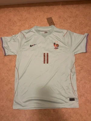 Frankrike VM-tröja 2026 Olise #11 - Ljusblå fotbollströja för VM 2026 från Nike med Frankrikes landslagsmärke och nummer 11 på bröstet. Namnet Olise och nummer 11 på ryggen. Tröjan har korta ärmar med ränder i blått, vitt och rött vid ärmsluten samt tunna röda detaljer längs sidorna. Perfekt för fotbollsfans! Passade inte mig därav säljer jag den, pris kan diskuteras vid snabb affär!