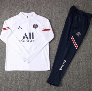 PSG träningsset vit och marinblå - Snyggt PSG träningsset med vit långärmad tröja med dragkedja och marinblå byxor. Tröjan har röda och svarta detaljer, PSG-logga och Jordan-logga. Byxorna har PSG-märke och texten 'PARIS' längs benet. Perfekt för fotbollsträning.