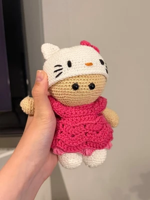Handvirkad amigurumi - Söt handvirkad docka med beige kropp, rosa klänning och vit Hello Kitty-inspirerad mössa i bomullsgarn. Pris är för material+arbetstid