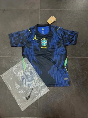 Blå Brasilien matchtröja Nike - Snygg blå och svart matchtröja från Nike med Brasilien-emblem på bröstet och gula detaljer. Tröjan har korta ärmar, rund hals och ett modernt mönster i blått och svart. Perfekt för fotbollsträning eller att bära till vardags.