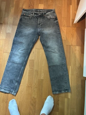 Grå raka jeans från WEEKDAY - Säljer ett par grå raka jeans från WEEKDAY med klassisk femficksdesign och diskreta slitningar. Jeansen har en vintagekänsla och är tillverkade i bomull. Perfekta för en avslappnad och stilren look.
