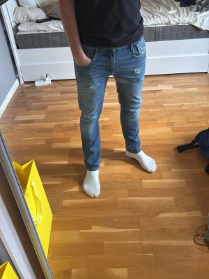 Replay jeans slitningar - Säljer ett par slim fit blå jeans med slitningar på låren och knäna. Jeansen har klassisk femficksdesign och normal midja. Perfekta för en avslappnad och trendig look.