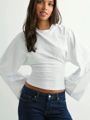 Vit croppad topp med vida ärmar - Snygg vit croppad topp med långa, vida ärmar och tight passform i midjan. Toppen har en enkel och clean look som passar perfekt till jeans eller kjol. Tillverkad i mjukt bomullsmaterial för en bekväm känsla.
