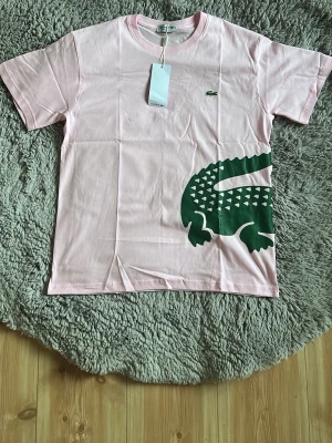 Lacoste T-shirt baby rosa  - En unik baby rosa lacoste tröja med en krokodil runt magen som sticker ut perfekt under sommaren 