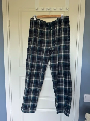 Rutiga pyjamasbyxor i bomull - Mysiga pyjamasbyxor med blå/grön, grå och vita rutor. Byxorna har resår i midjan med snörning. Tillverkade i mjuk bomull, perfekta för slappa dagar hemma. Säljer eftersom de blivit för små för mig. 