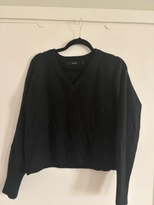 Svart stickad V-ringad tröja - Säljer en svart stickad tröja från Vero Moda med V-ringning och långa ärmar. Tröjan har en avslappnad passform och ribbade muddar vid ärmslut och nederkant. Perfekt att matcha med jeans eller kjol för en enkel och snygg look.