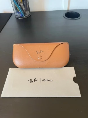 Ray-Ban Meta svarta smarta glasögon - Säljer ett par svarta smarta glasögon från Ray-Ban i samarbete med Meta. Klassisk Wayfarer-form med robust plastbåge och inbyggd teknik. Kommer med ett snyggt brunt fodral i läder och originalförpackning. Perfekt för dig som vill ha stil och smarta funktioner i ett.