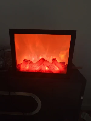 Elektrisk dekorationseld i svart ram - Snygg elektrisk dekorationseld med svart fyrkantig ram. Elden har en realistisk glödeffekt med orange och röda toner som ger mysig stämning. Perfekt som inredningsdetalj för att skapa värme och atmosfär i rummet. Drivs med el och är enkel att placera.