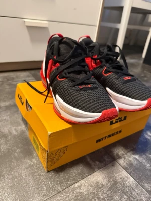 Nike LeBron Witness 7 svart/röd - Snygga Nike LeBron Witness 7 sneakers i svart mesh med röda och vita detaljer. Skorna har en tydlig Air Max-sula, vit Swoosh-logga och LeBron-detaljer. Dem är helt nya, Ny pris 1671kr
