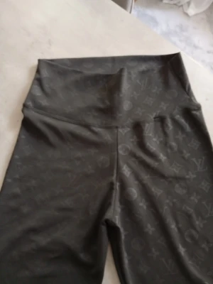 Svarta leggings med monogrammönster - Snygga svarta leggings med högt midjeband och klassiskt L√-monogram över hela tyget. Materialet är stretchigt och följsamt, perfekt för en trendig och bekväm look. Passar dig som gillar exklusiva och stilrena plagg. Står XL men upplever dom som M/L