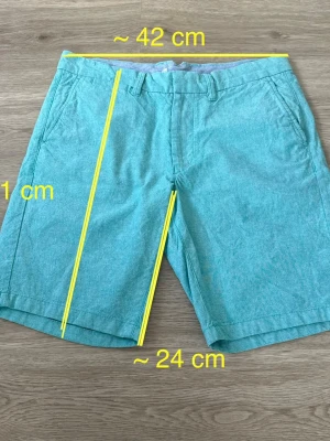 Turkosa chinosshorts från Dressmann i S - Snygga turkosa shorts i S med klassisk passform. Färgen är en aning åt det solblekta hållet men så har den alltid varit. I mycket bra skick - nyskick. Se bild för mått.
