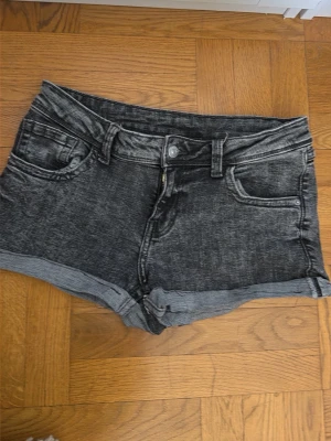 Svarta denimshorts med upprullad kant - Säljer ett par svarta denimshorts med upprullad kant och klassisk femficksdesign. Shortsen har bälteshällor, knapp och dragkedja framtill samt en tvättad look för en avslappnad stil. Har gjort om dom från ett par jeans till ett par shorts💕