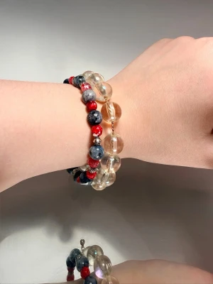 Två pärlarmband i färg och glas - Säljer två snygga armband med pärlor. Ett armband har stora, transparenta glaspärlor med guldfärgat spänne. Det andra har mindre pärlor i blått, rött och silver, med coolt mönster. 