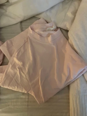 Ljusrosa t-shirt med knyt där bak - En stilren ljusrosa t-shirt med knyt där bak och korta ärmar. T-shirten är i mjuk bomull och har en enkel, clean look som passar till det mesta. Perfekt för dig som gillar minimalistisk stil. Priset kan diskuteras 
