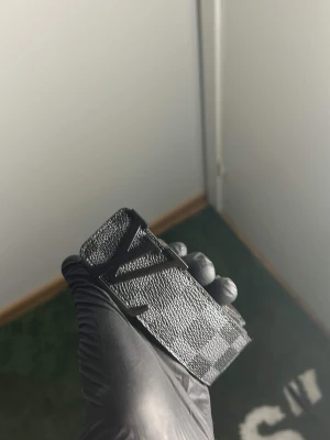 Svart  bälte med rutigt mönster - Snyggt svart bälte med klassiskt rutigt mönster och stor -logga i metall som spänne. Bältet har en lyxig känsla och insidan är i ljusbrunt skinn. Perfekt accessoar för att lyfta din outfit.