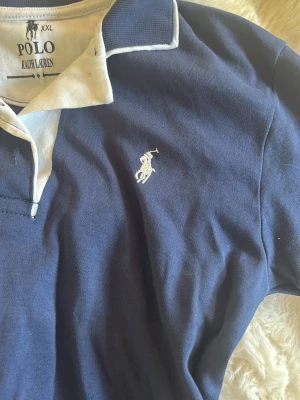 Marinblå pikétröja från  Ralph Lauren - Högst troligen inte äkta då jag köpte utomlands , står att den är xxl men passar mig som är Xs - S . Klassisk marinblå pikétröja från Polo Ralph Lauren med vit broderad logga på bröstet och kontrasterande vit krage. Tröjan har korta ärmar och knappar vid halsen. Tillverkad i mjuk bomull för en bekväm känsla.