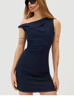 Mörkblå  jeansklänning - Snygg mörkblå jeansklänning från Bershka med asymmetrisk axel och figurnära passform. Klänningen är ärmlös och har en cool, modern look med en axel bar. Tillverkad i denimtyg som ger en trendig känsla.