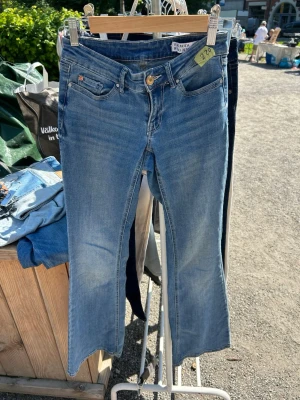 Blå bootcut jeans från Vero Moda - Snygga blå bootcut jeans från Vero Moda i klassisk denim. Jeansen har fem fickor, gylf med dragkedja och knapp samt lätt slitna detaljer framtill för en trendig look. Perfekta för dig som gillar en avslappnad men stilren stil.