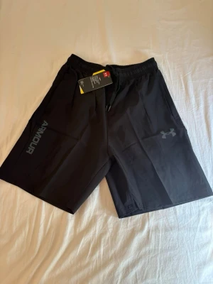 Under Armour Shorts - M men passar S - Säljer ett par snygga och bekväma träningsshorts från Under Armour. Lätt och snabbtorkande material som passar perfekt för gym, löpning, padel eller annan träning. Resår i midjan med justerbar dragsko för optimal passform.  ✔️ Storlek: M ✔️ Skick: Helt nya med prislappar kvar ✔️ Färg: Svart ✔️ Lätt, ventilerande och bekvämt material  Hör gärna av dig om du har frågor eller vill ha fler bilder!  