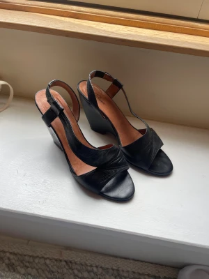 Svarta kilklackade sandaler i skinn - Säljer ett par skitsnygga svarta klackar med kilklack och öppen tå. Dom är från NK (Rizzo) finns inte att köpa längre. Nypris ca 2500 kr💕skriv om du vill ha mer information eller fler bilder!