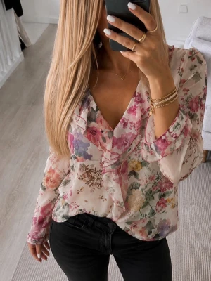 Blommig volangblus från Zara - Snygg blus från Zara med blommigt mönster i rosa, lila, gult och grönt. Blusen har volangdetaljer längs den djupa v-ringningen och är tillverkad i ett tunt, transparent material. Långärmad modell som ger en luftig och feminin känsla.