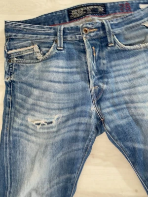Slitna Replay jeans - Jeansen är väldigt slitna, alla slitningar är inte en del av designen, men slitningarna som finns ser du på bilden, utöver lite småsaker längst ner på benen. Slitningar skapar karaktär och är perfekt för dig som vill sticka ut lite. Jeansen är slim/regular typ.  Storlek: W28 L32. Märket är replay. Jeansen är mycket mjuka och bekväma, vid minsta fundering är det bara att fråga.