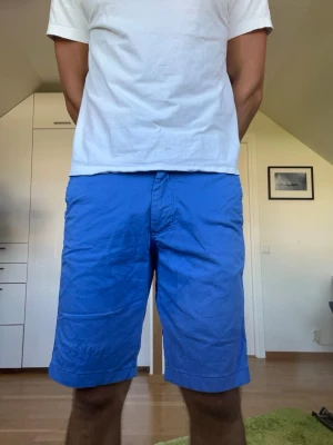 Blåa shorts i bomull - Blåa shorts från Morris i 97% bomull. Strl 32. Inga defekter. Följer med en extraknapp. Modellen är 178 cm och väger 77kg. Hör gärna av dig vid frågor!