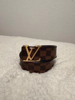 bälte – Damier Ebene | Tidlös & Exklusiv 🔥 - Säljer ett stilrent -bälte i den klassiska Damier Ebene-designen med den ikoniska -spännet i guldfinish. Ett lyxigt tillbehör som passar perfekt till både jeans, kostymbyxor och mer uppklädda outfits.