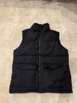 Svart dunväst  - Hej! Säljer en snygg svart dunväst med hög krage och dragkedja framtill. Nyskick utan defekter 👍storlek M. Priset ej fast 🙌