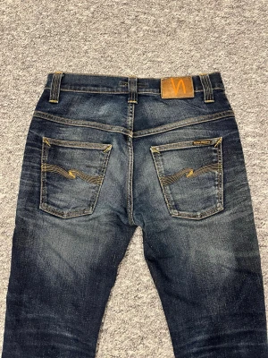 Mörkblå jeans från Nudie Jeans - Säljer ett par mörkblå jeans från Nudie Jeans med snygga slitningar. Jeansen lite tvätt märken vilket gör dem perfekta. Det står att det är storlek W30 och L 34 men det är w31 o L32 