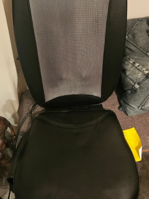 Massagekudde med fjärrkontroll - Elektrisk massagekudde i svart konstläder och grått tyg, perfekt för rygg och säte. Medföljande fjärrkontroll har flera inställningar för styrka och zoner (övre, nedre, hel rygg). Enkel att använda hemma eller på kontoret.