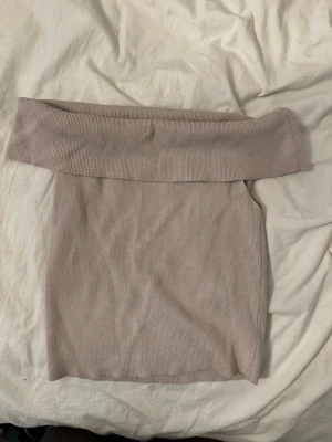 Ljusbeige ribbad topp - Snygg beige tubtopp med bred offshoulder-krage och ribbad struktur. Toppen är ärmlös och har en mjuk, stretchig känsla som sitter skönt på kroppen. Perfekt att matcha med höga jeans eller kjol för en trendig look.