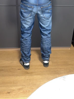 Blå Gstar jeans med slitningar - Säljer ett par blå jeans från Gstar med snygga slitningar och tvättade detaljer. Jeansen har raka ben, klassiska fem fickor och kontrastsömmar. Perfekta för en avslappnad streetstil och passar till sneakers. Materialet är denim i bomull. Dessa går inte att få tag på, är vintage modell, pris är bara att föreslå! Har inget satt pris så utgå inte ifrån startprisey